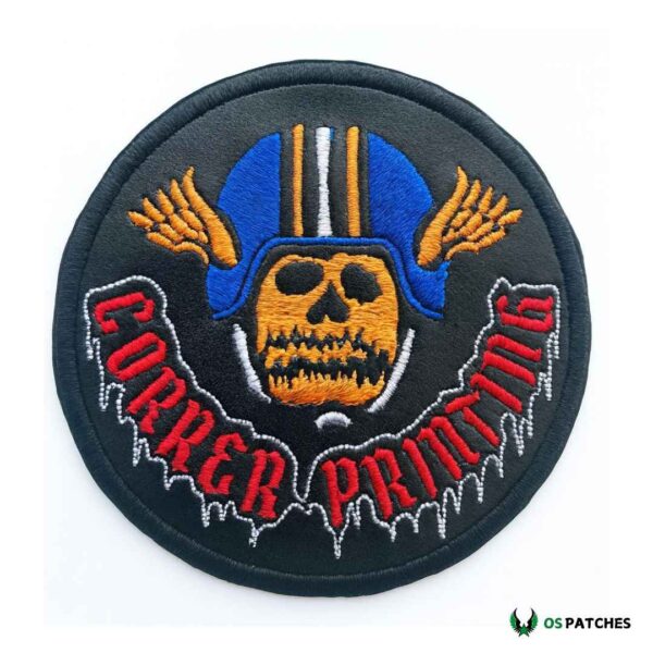 Round black leather patch with embroidered orange skull wearing blue helmet with wings and red text “CORRER PRMMG.”