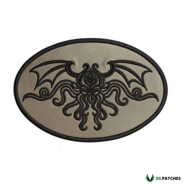 Oval grey leather patch with embroidered black Cthulhu-style creature with wings and tentacles.